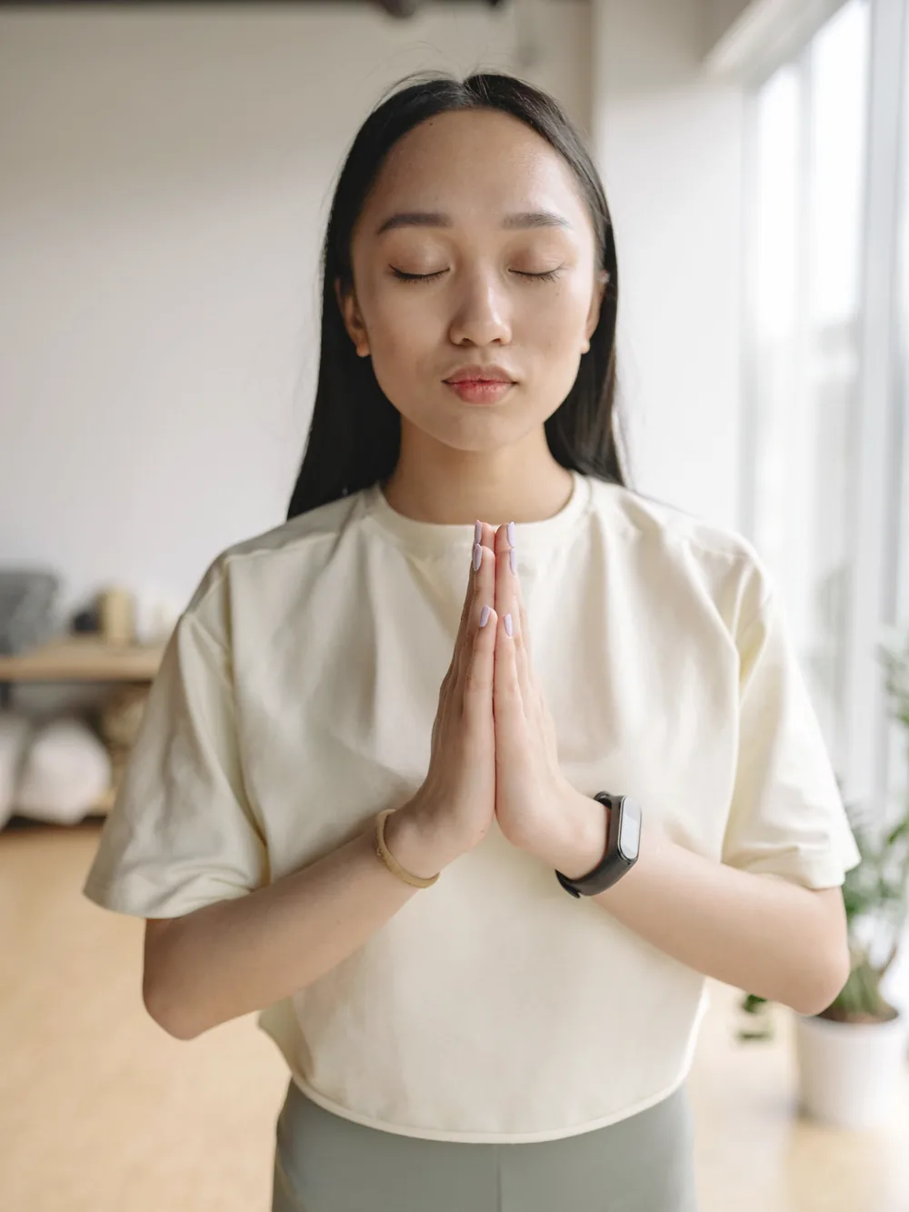 窓の光の中で、胸の前で手を合わせて目を閉じる女性