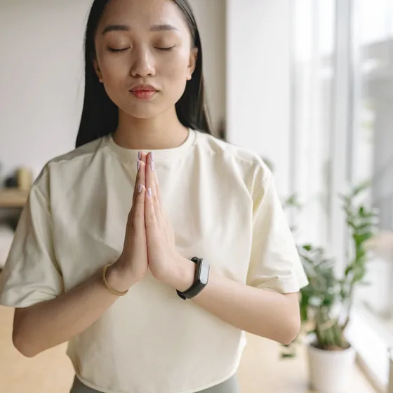 窓の前で背筋を伸ばして立ち、胸の前で手を合わせる女性