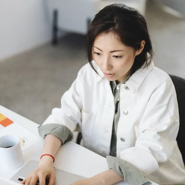 白いシャツで、ノートパソコンに向かって作業する女性