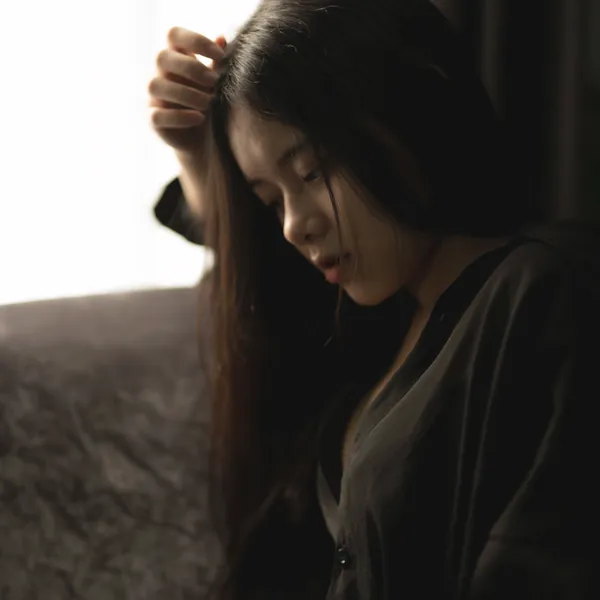 暗い部屋で髪に手をやり、うつむく女性