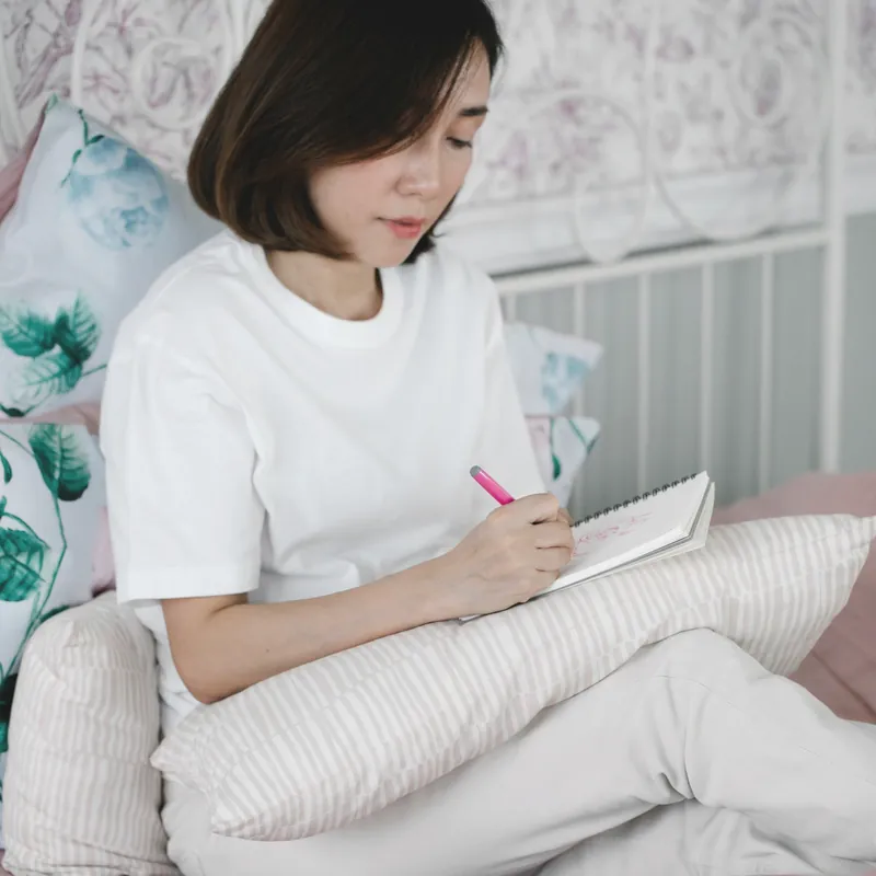 白いTシャツでベッドに座り、ノートに書きこむ女性