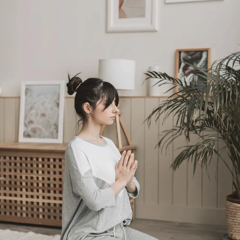部屋着で膝をつき、胸の前で手を合わせる女性