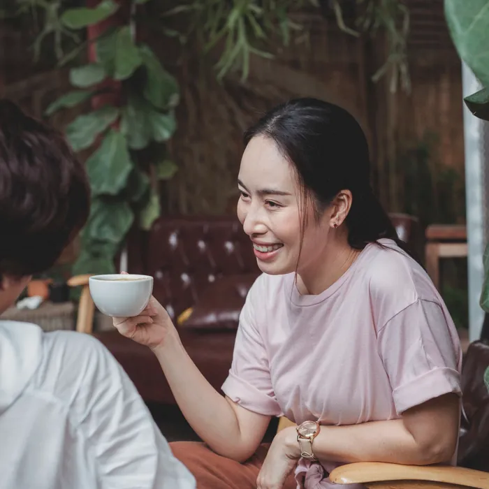 ピンクのTシャツの女性が、お茶を持って笑っている
